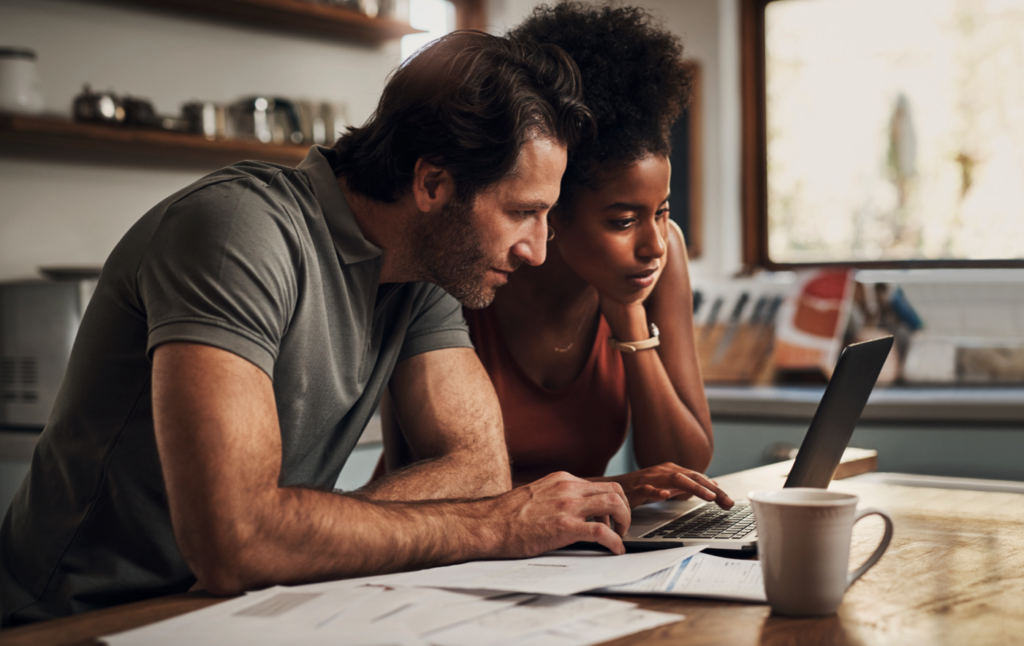 Two people sit at a table viewing a laptop computer screen together.